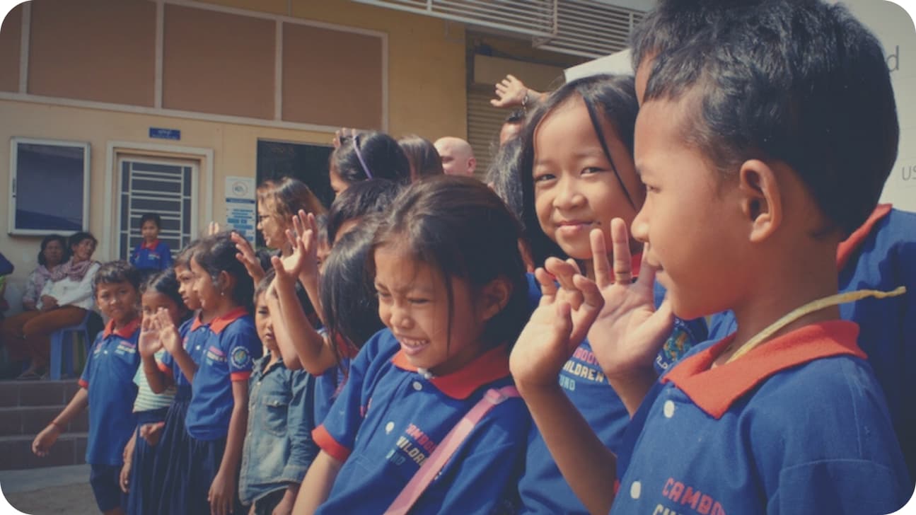 Children in Cambodian Children’s Fund uniforms clapping outside their school